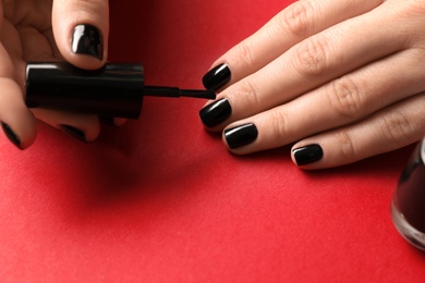 Woman applying black nail polish on color background, closeup