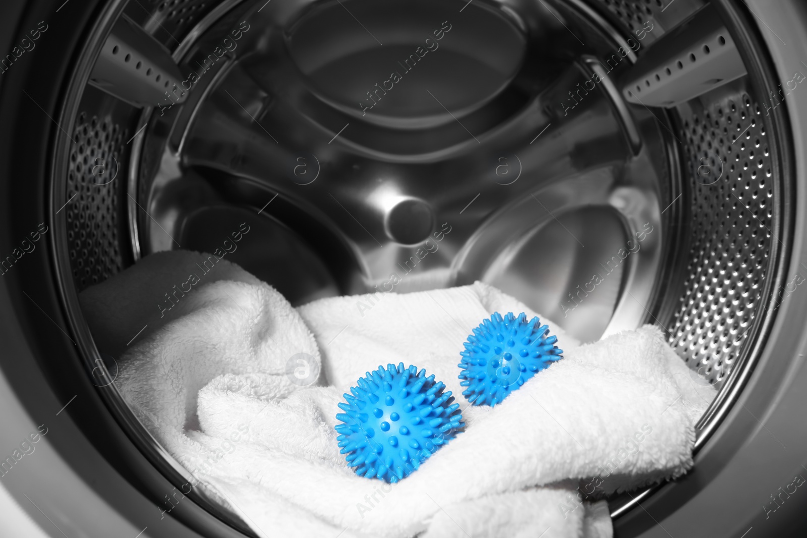 Photo of Blue dryer balls and towel in washing machine drum, closeup