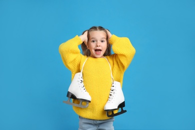 Photo of Excited little girl in yellow knitted sweater with ice skates on blue background