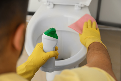 Photo of Man cleaning toilet bowl in bathroom, closeup