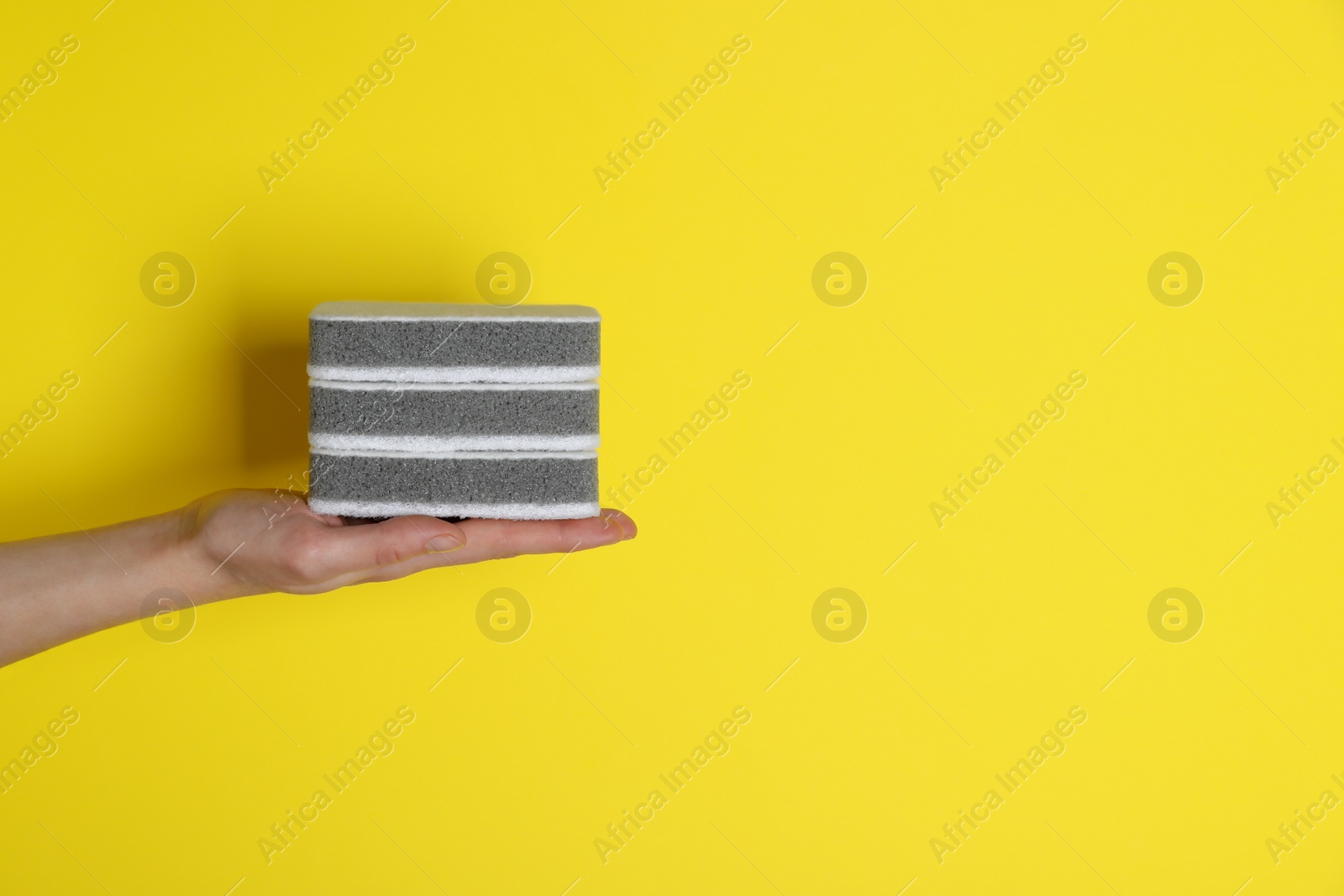 Photo of Woman holding sponges on yellow background, closeup. Space for text