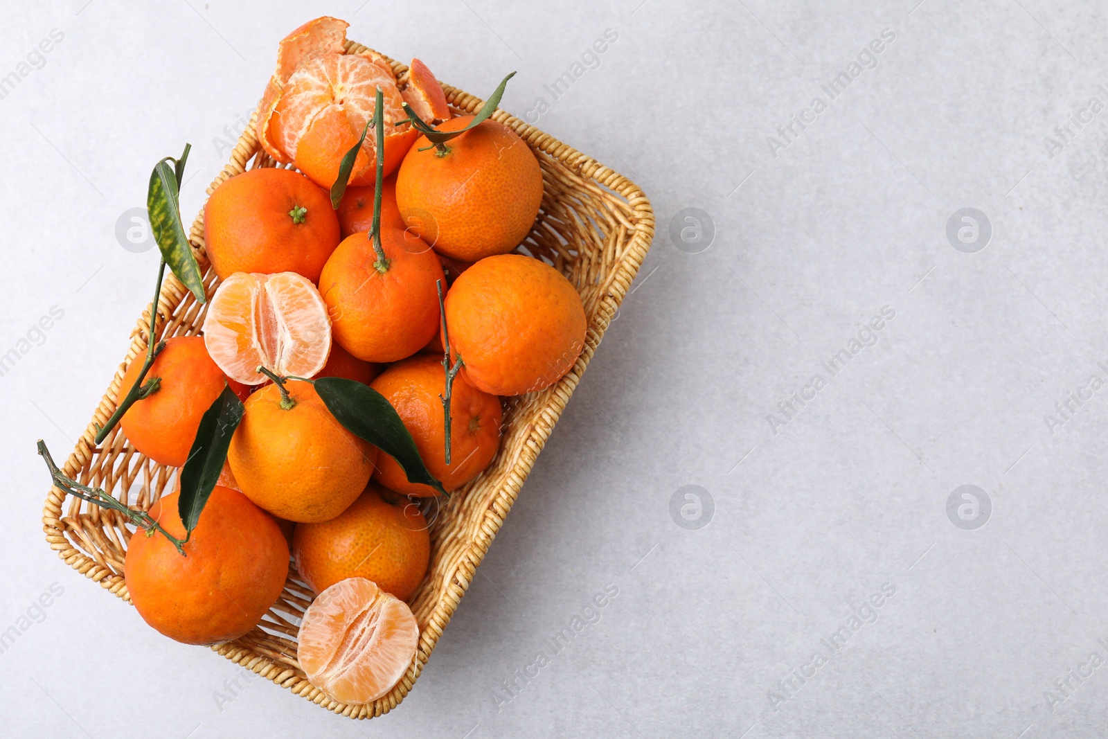 Photo of Fresh ripe tangerines with green leaves in wicker basket on white table, top view. Space for text