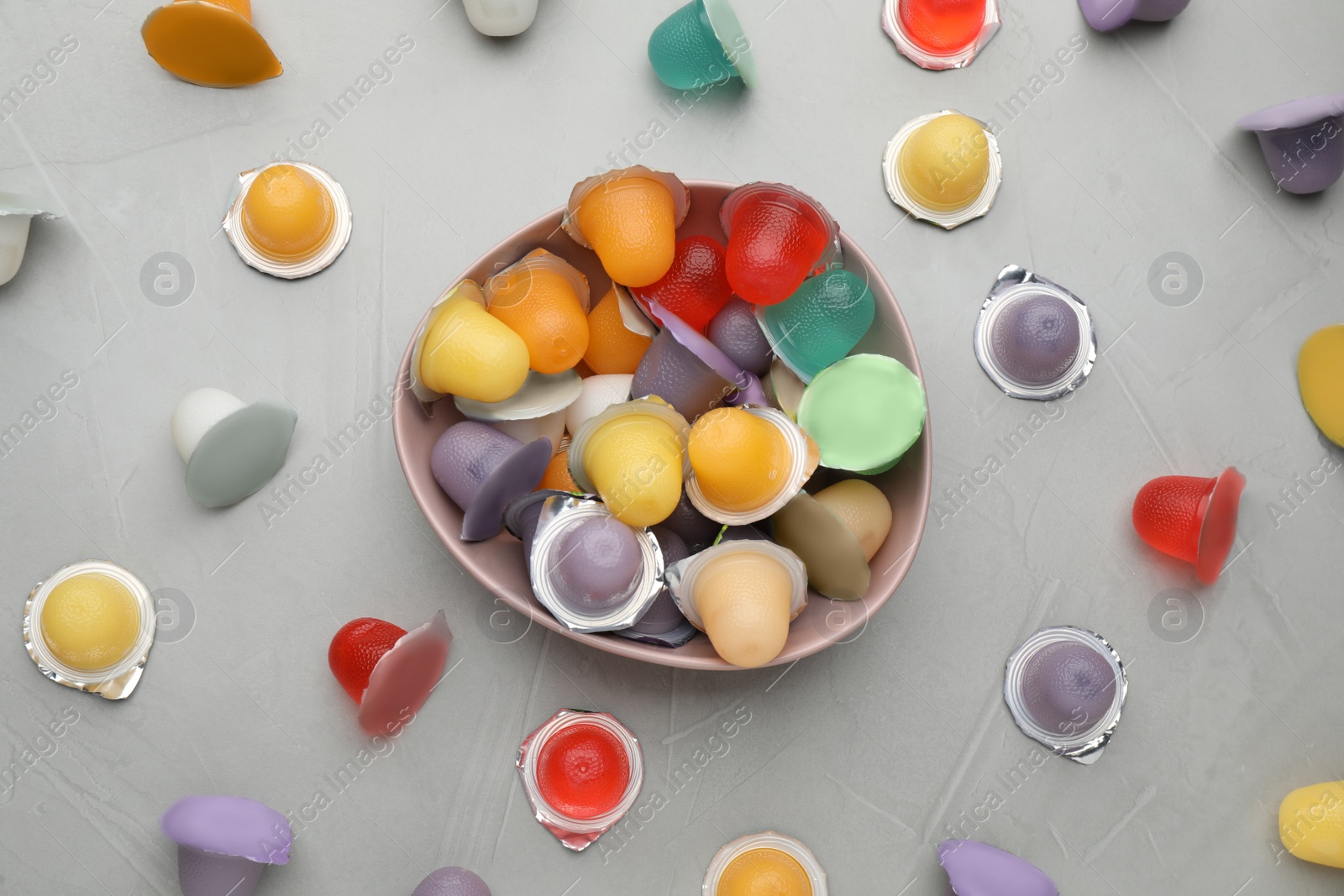 Photo of Bowl with tasty bright jelly cups on light table, flat lay