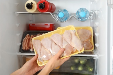 Photo of Woman taking raw chicken drumsticks from refrigerator, closeup