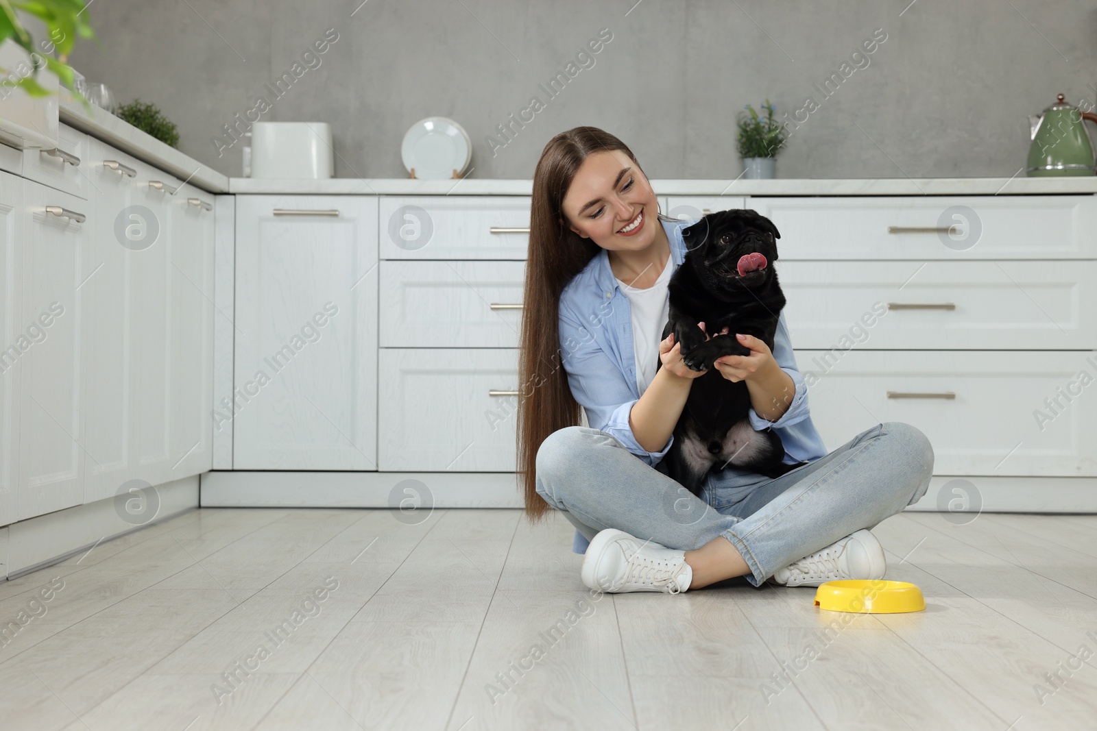 Photo of Beautiful young woman holding her adorable Pug dog in kitchen, space for text