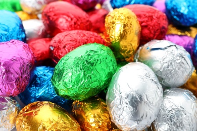 Photo of Many chocolate eggs wrapped in bright foil as background, closeup view