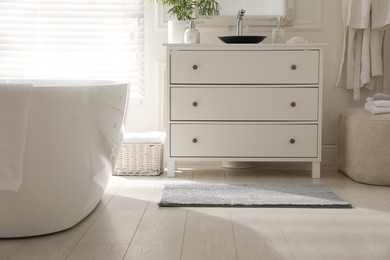 Photo of Stylish grey mat near chest of drawers in bathroom