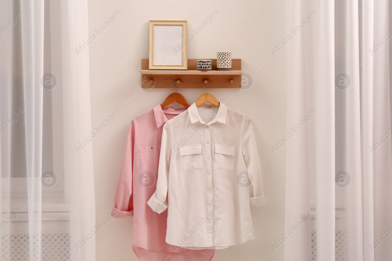 Photo of Wooden shelf with fashionable clothes and decorative elements on light wall in room. Interior design