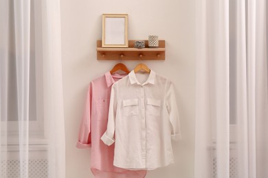 Wooden shelf with fashionable clothes and decorative elements on light wall in room. Interior design