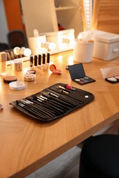 Photo of Set of makeup brushes and cosmetics on wooden table in room
