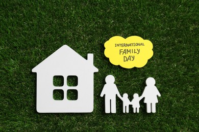 Photo of Card with text International Family Day and wooden figures on green grass, flat lay