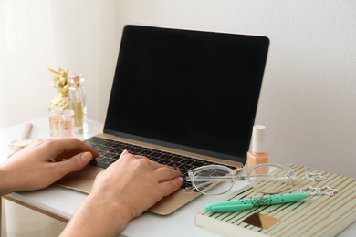 Photo of Woman with cosmetic products using laptop at table, closeup. Beauty blogger