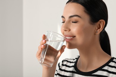 Photo of Young woman drinking water indoors, closeup. Refreshing drink. Space for text.