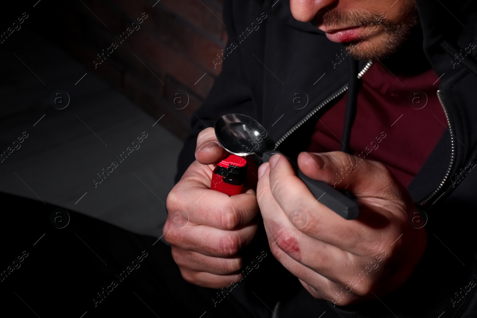 Photo of Man preparing drug with spoon and lighter near brick wall, closeup