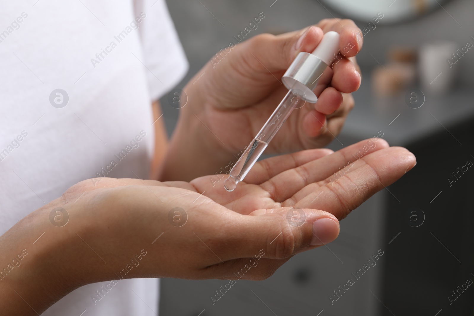 Photo of Woman applying cosmetic serum onto her hand indoors, closeup