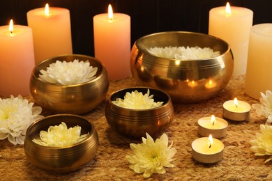 Photo of Tibetan singing bowls with beautiful flowers and burning candles on table