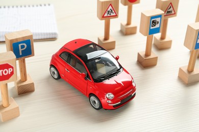 Photo of Many different miniature road signs and car on white wooden table. Driving school
