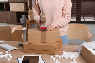 Photo of Seller taping parcel at table in office, closeup