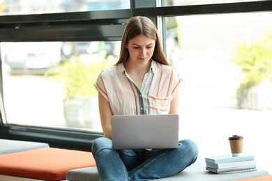 Young woman working on laptop near window in library