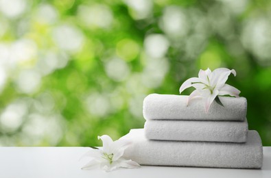 Spa holiday. Stack of fresh towels with flowers on table against blurred green background, space for text