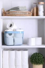 Toilet paper rolls, floral decor, cotton pads and towels on white shelves