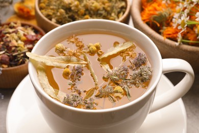 Photo of Cup of aromatic freshly brewed tea and different dry herbs on table, closeup