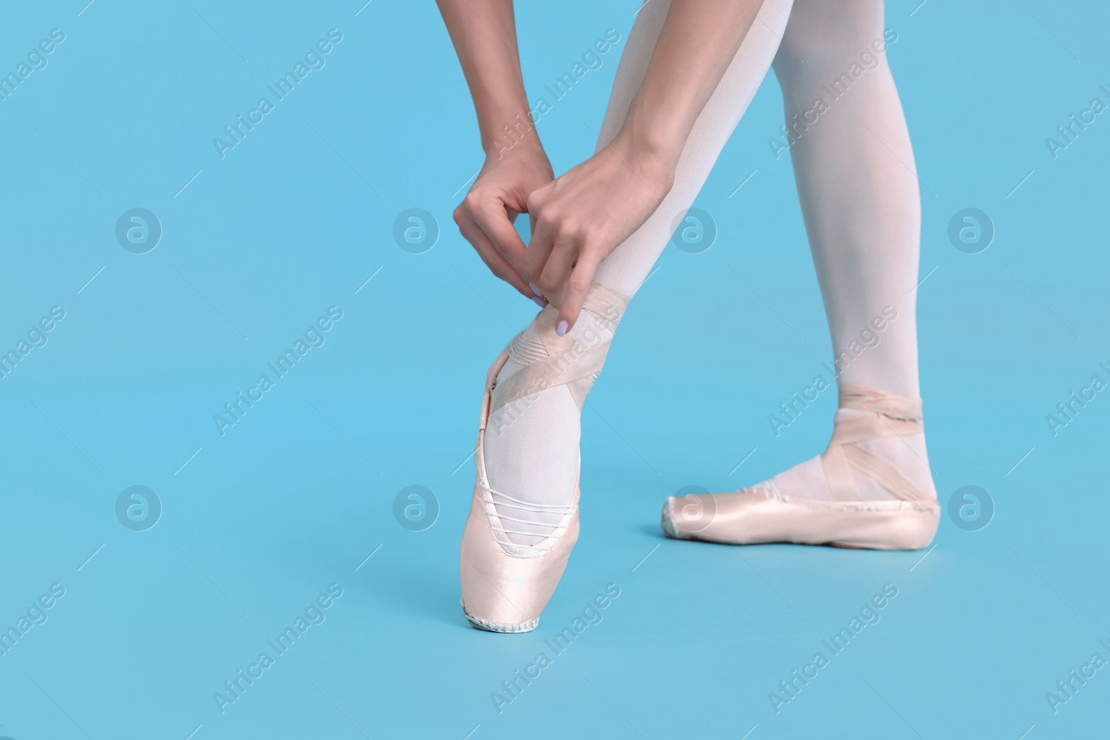 Photo of Young ballerina tying pointe shoes on light blue background, closeup