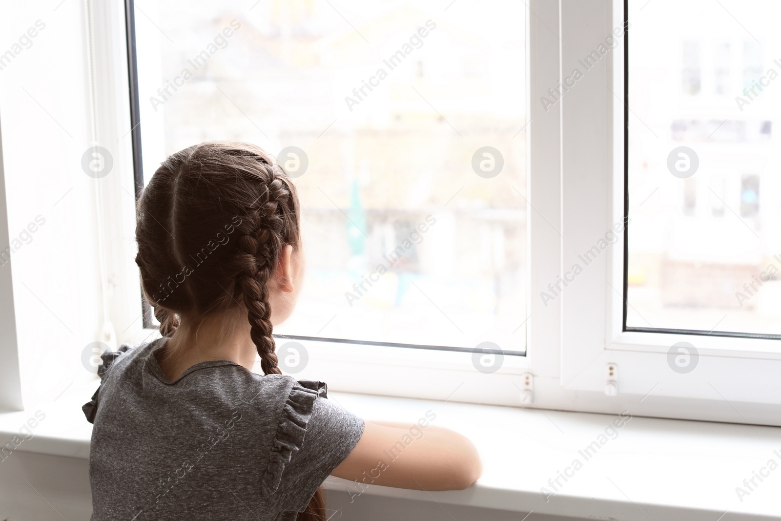 Photo of Lonely little girl near window indoors. Child autism