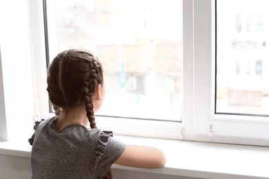 Lonely little girl near window indoors. Child autism