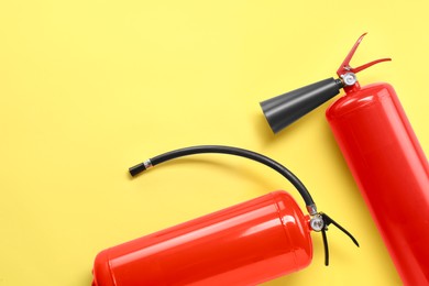 Two fire extinguishers on yellow background, flat lay. Space for text