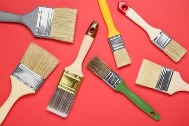 Photo of Many different paint brushes on red background, flat lay