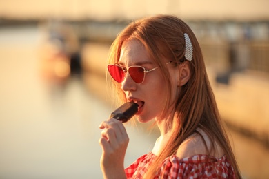 Beautiful young woman with ice cream outdoors at sunset