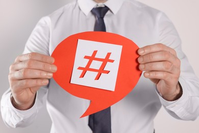 Photo of Man holding paper speech bubble with hashtag symbol on light background, closeup