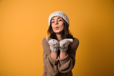 Photo of Young woman in warm sweater, hat and mittens on yellow background. Christmas season