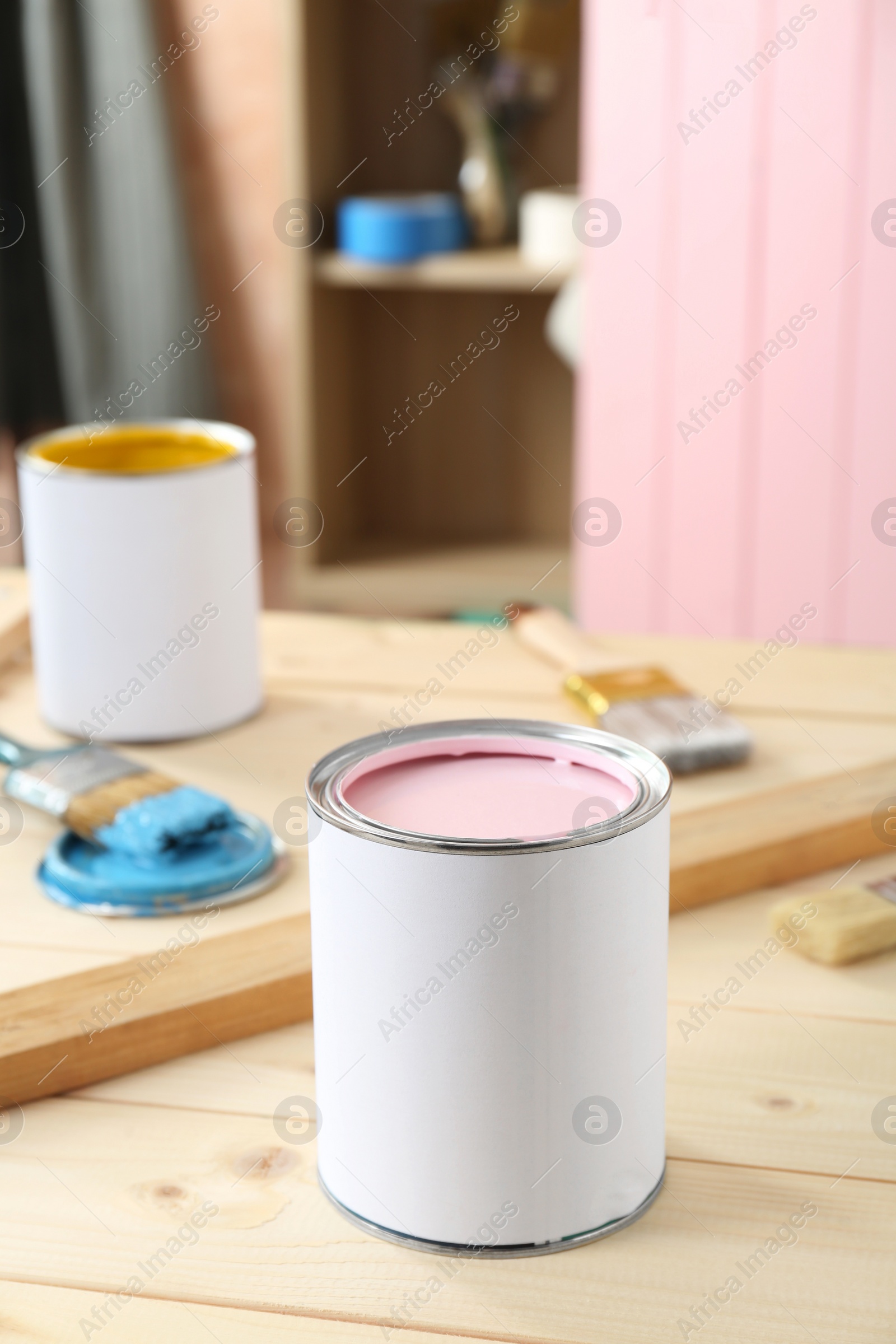 Photo of Cans of colorful paints and brushes on wooden table indoors