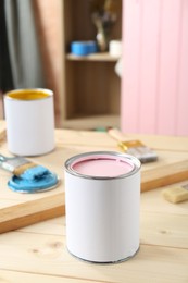 Photo of Cans of colorful paints and brushes on wooden table indoors