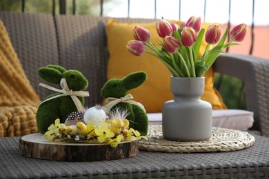 Photo of Terrace with Easter decorations. Bouquet of tulips in vase, bunny figures, decorative nest and eggs on table outdoors