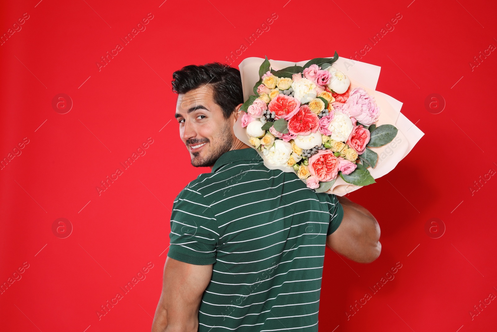 Photo of Young handsome man with beautiful flower bouquet on red background