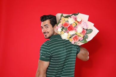 Young handsome man with beautiful flower bouquet on red background