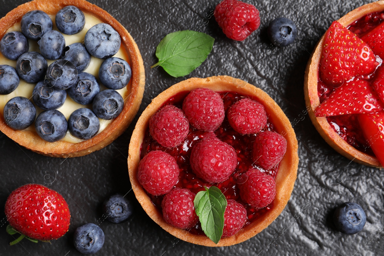 Photo of Tartlets with different fresh berries on black table, flat lay. Delicious dessert