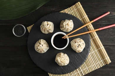 Slate plate with tasty baozi dumplings, chopsticks and soy sauce served on wooden table, top view