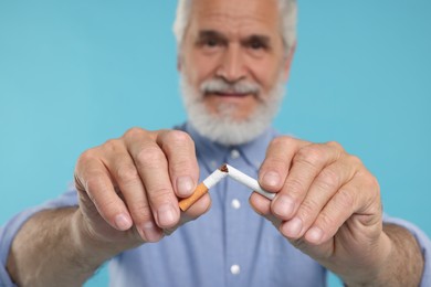 Stop smoking concept. Senior man breaking cigarette on light blue background, selective focus