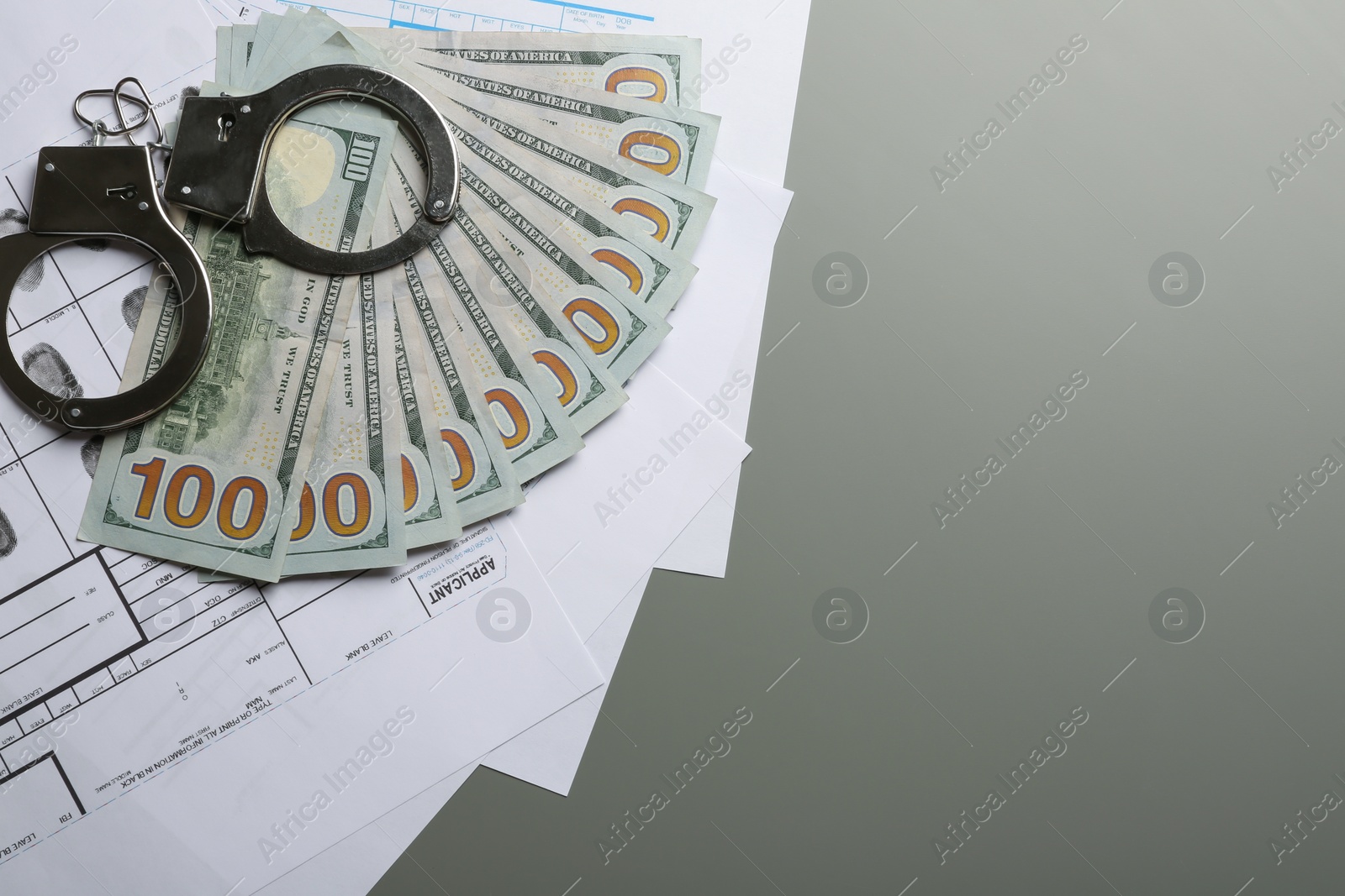 Photo of Money, handcuffs and fingerprint record sheets on grey background, top view with space for text. Criminal investigation