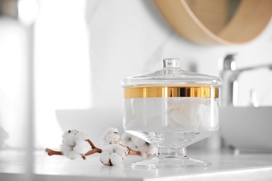 Jar with cotton pads and flowers on countertop in bathroom