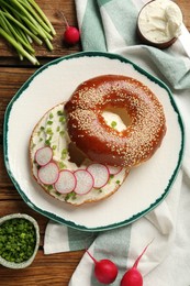 Photo of Delicious bagel with cream cheese, green onion and radish on wooden table, flat lay