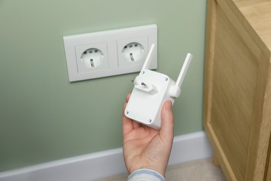 Woman holding wireless Wi-Fi repeater indoors, closeup