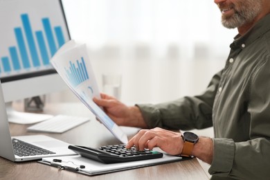 Professional accountant using calculator at wooden desk in office, closeup