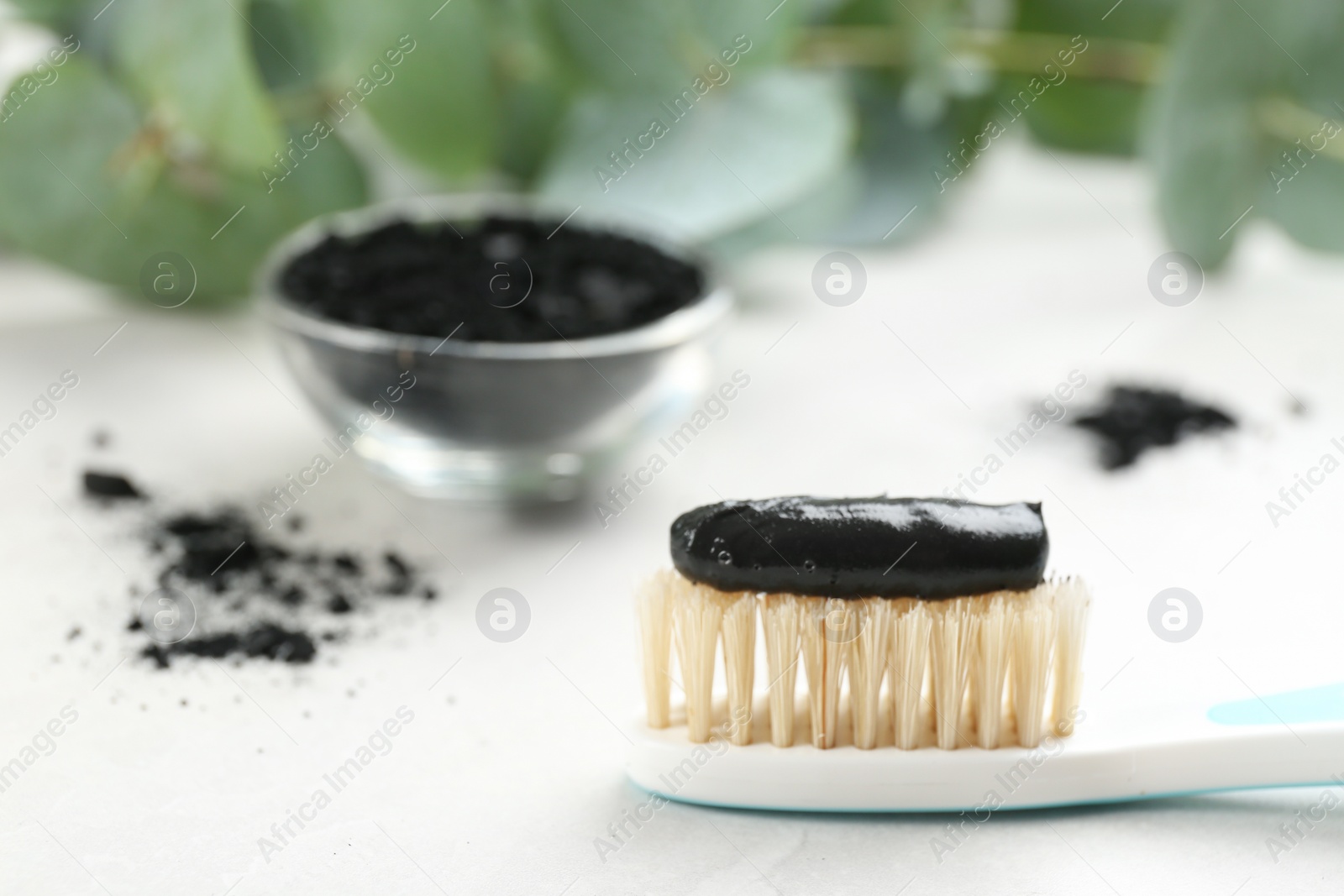 Photo of Toothbrush with natural bristles and charcoal paste on white table, closeup. Space for text