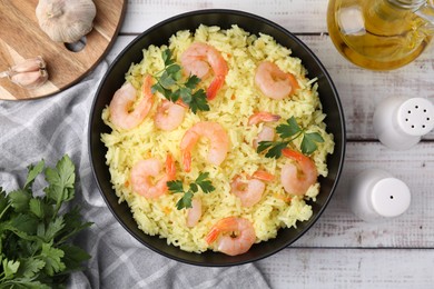 Delicious risotto with shrimps and parsley served on white wooden table, flat lay