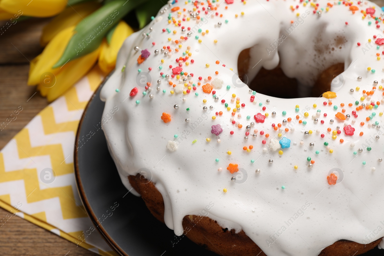 Photo of Easter cake with sprinkles and tulips on wooden table, closeup